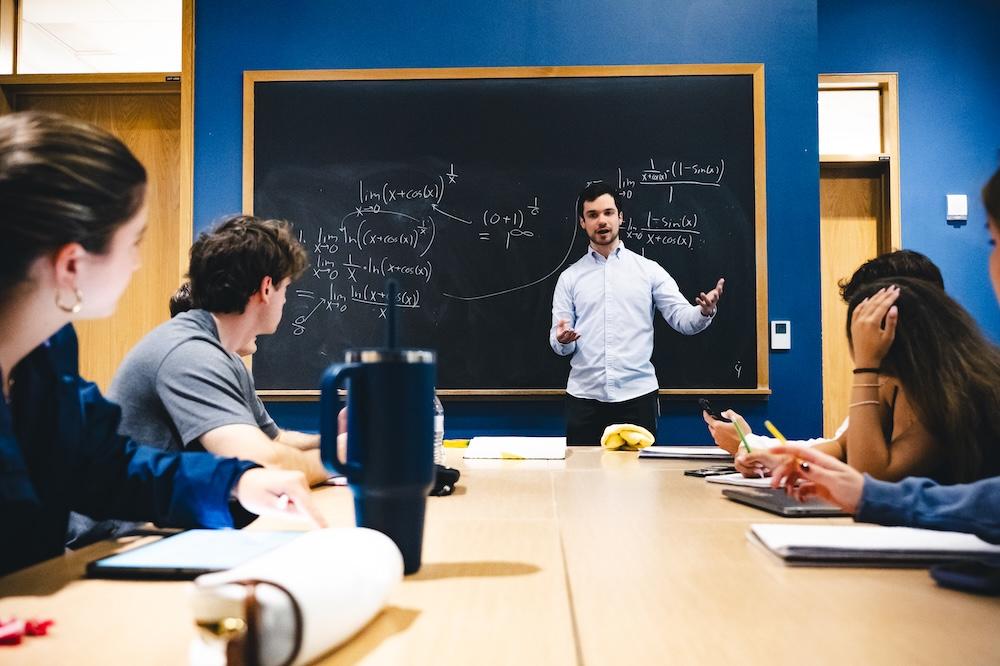 Isaac Reiter stands in front of a blackboard and tutors students.